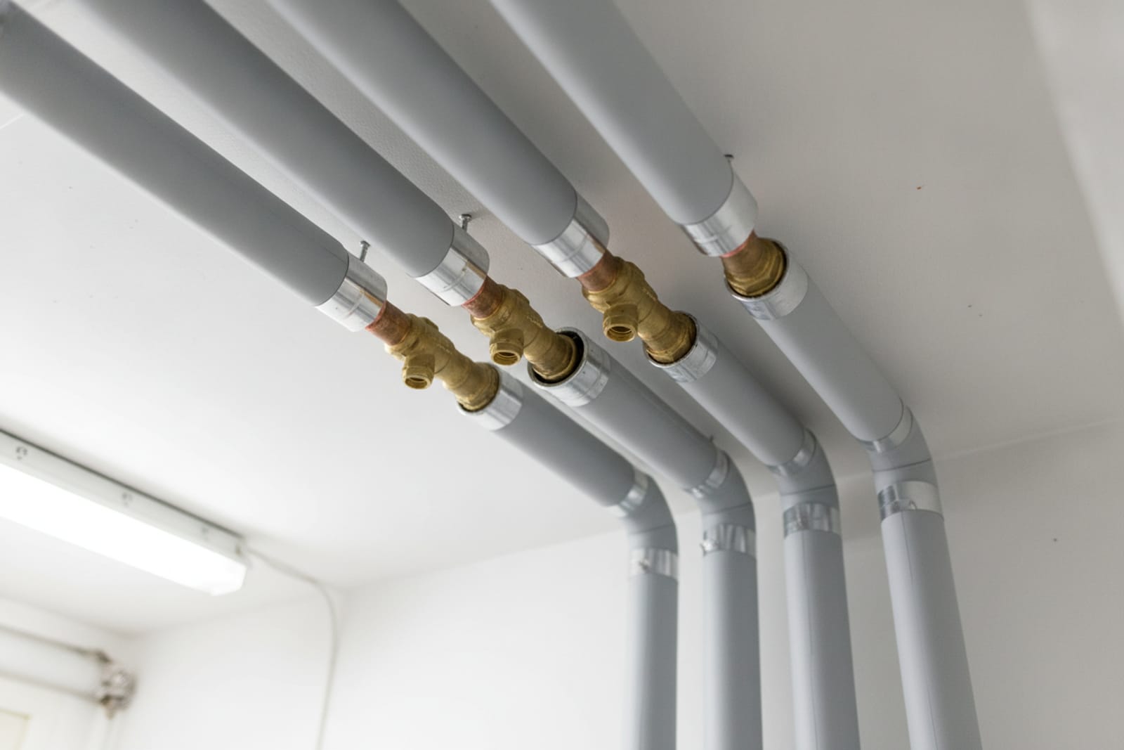 Rörstråk i tak isolerade med ljusgrå isolering och aluminiumband – kopparrör och mässingsventiler syns vid anslutningarna.